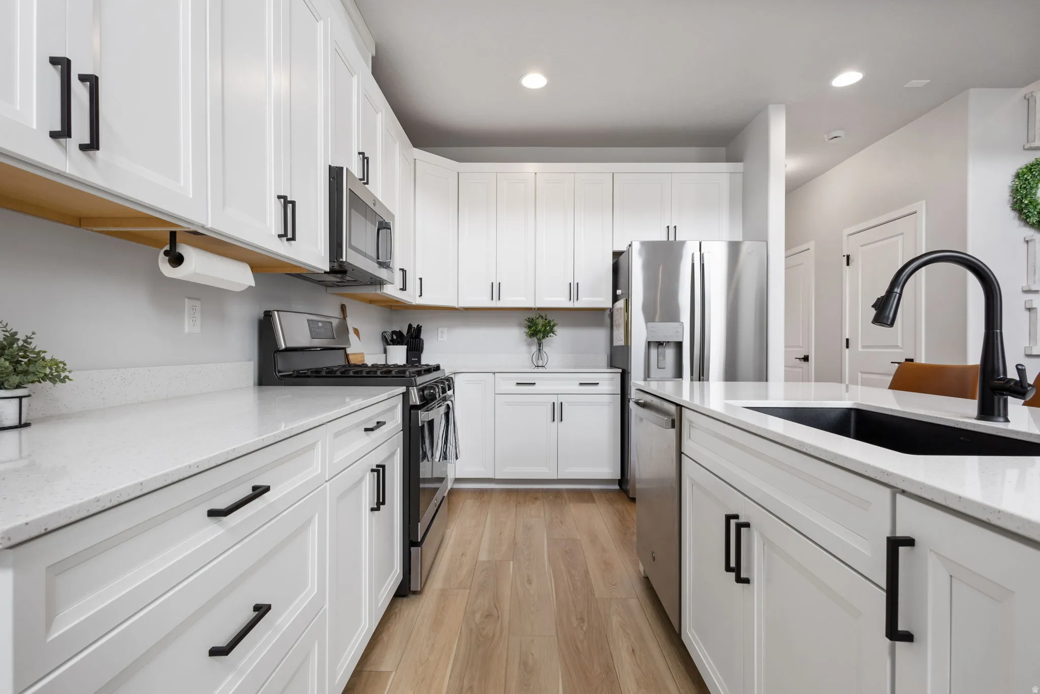 Modern kitchen featuring white shaker cabinetry with matte black hardware, light-toned countertops, stainless steel appliances, and wood-finish flooring