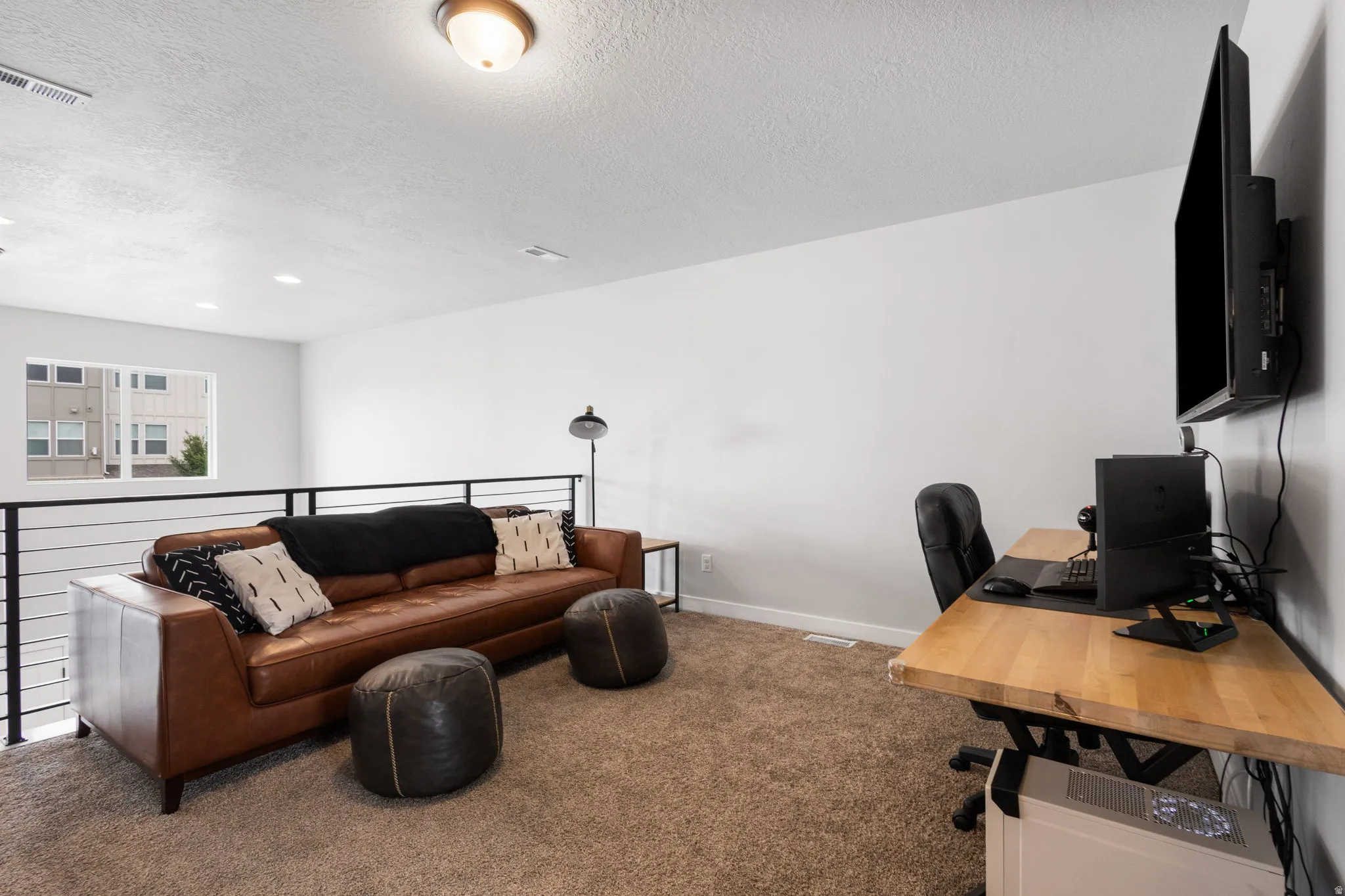 Carpeted loft space featuring a horizontal metal railing, white walls, and an overhead light fixture