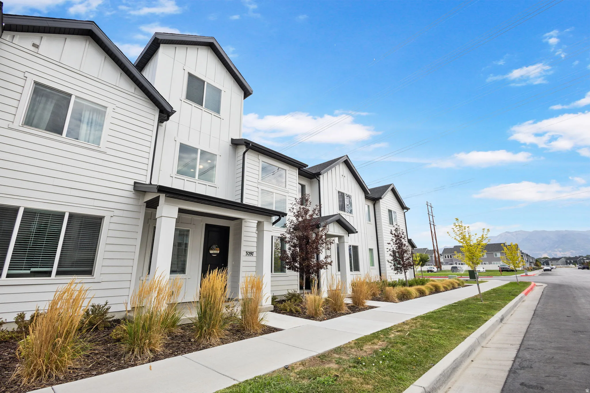 Modern townhome exterior featuring white siding with black trim, a covered entry porch, and mature landscaping