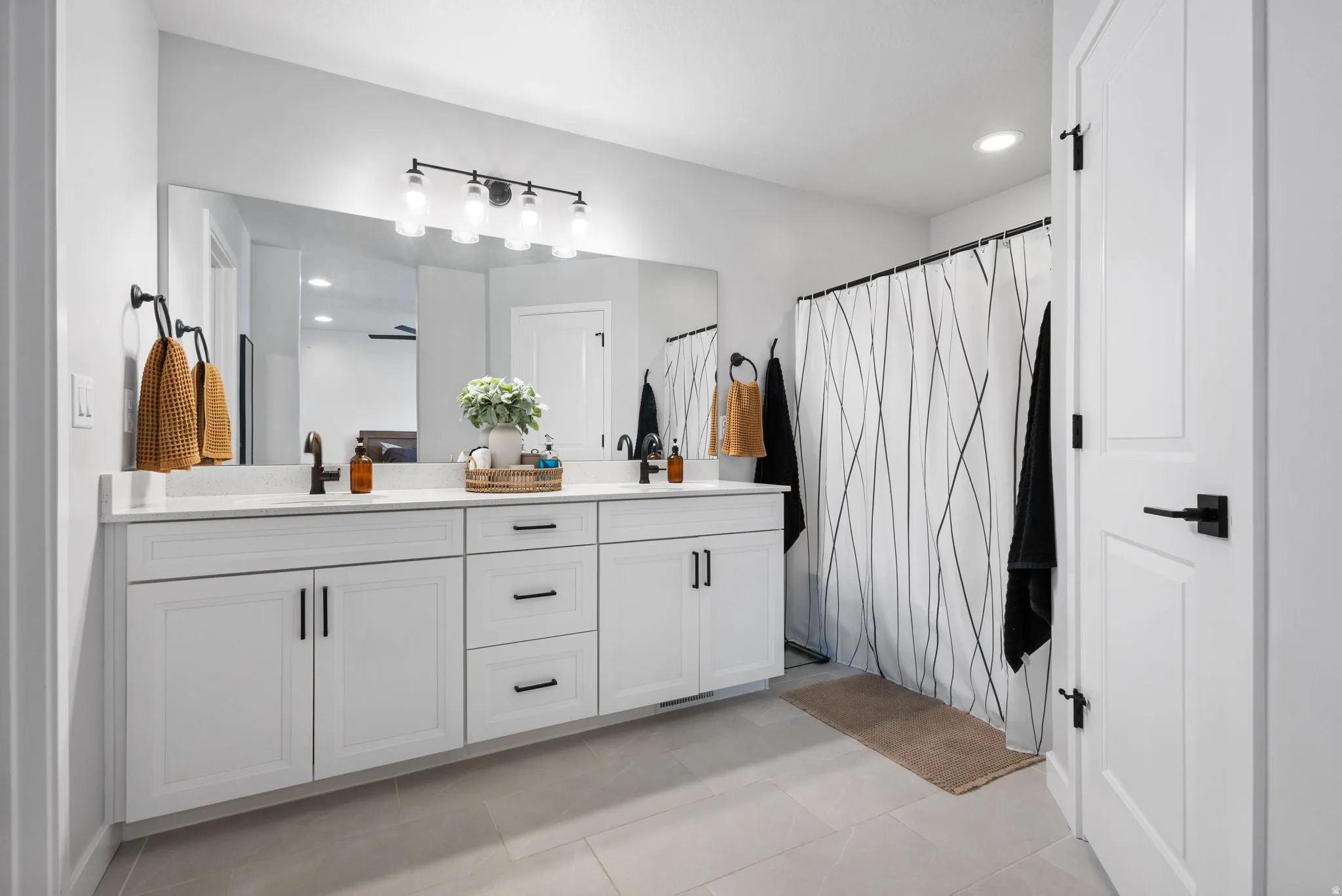 Dual vanity with white cabinetry, matte black hardware, and an expansive wall-mounted mirror