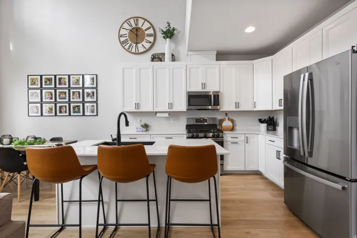 Contemporary kitchen featuring white cabinetry, stainless steel appliances, a center island with a black sink and faucet, light wood-finish flooring, and white countertops