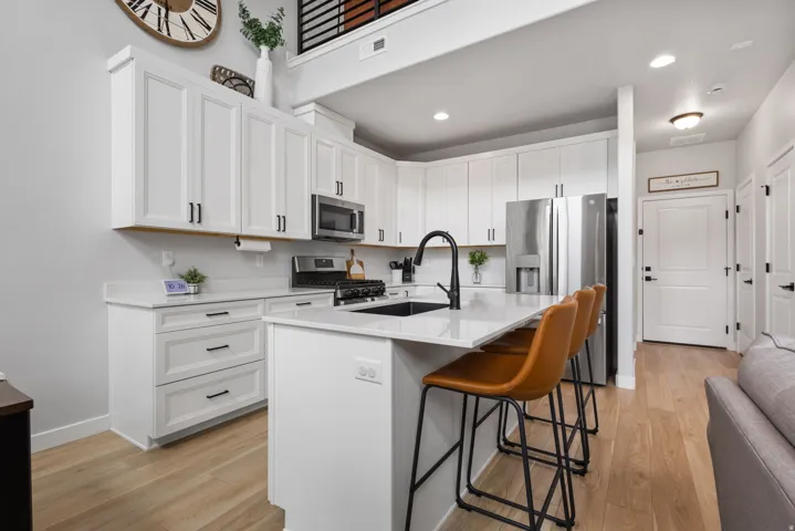 Contemporary kitchen featuring white cabinetry with black hardware, stainless steel appliances, a center island with seating, and wood-finish flooring