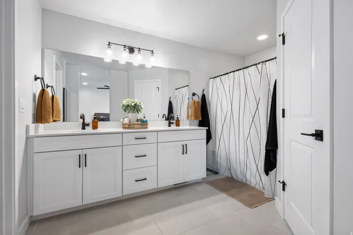 Dual vanity with white cabinetry, matte black hardware, and an expansive wall-mounted mirror