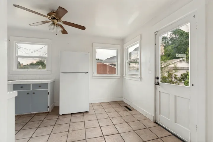 Bright, open kitchen featuring ceramic tile flooring, ample counter space with gray cabinetry, built-in refrigerator, and multiple windows providing natural light