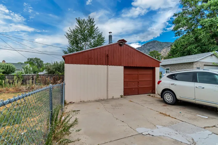 Detached garage featuring a red metal exterior with white panel siding, oversized red garage door, and concrete driveway apron