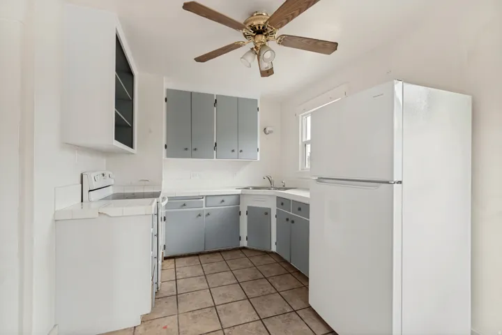 Efficient galley kitchen featuring gray cabinetry, stainless steel appliances including a refrigerator and range, laminate countertops, and ceramic tile flooring