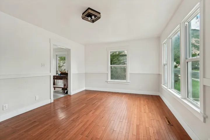 Spacious room featuring wood-finish flooring, white walls with a chair rail, multiple windows, and a flush mount ceiling light fixture
