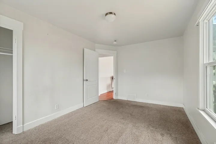 Carpeted room featuring a white interior door, a window with white trim, and a flush-mount ceiling light fixture