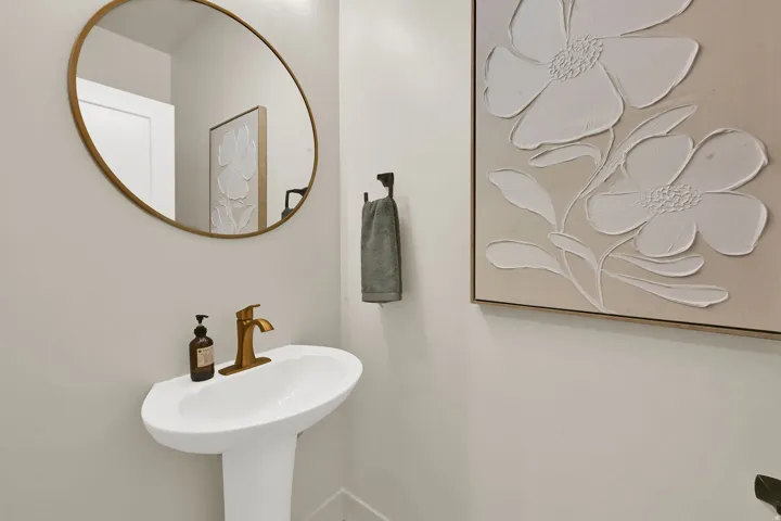 Pedestal sink with a gold-tone faucet, complemented by a round gold-framed mirror