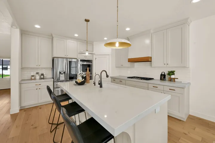 Modern kitchen featuring a large center island with integrated sink, stainless steel appliances, light wood-finish flooring, white subway tile backsplash, and recessed lighting