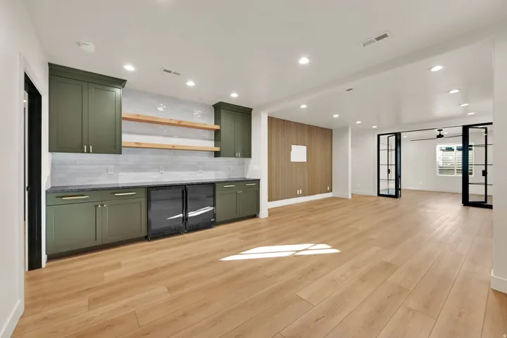 Spacious recreation room featuring wood-finish flooring, a built-in wet bar with olive-toned cabinetry, two beverage refrigerators, and a white subway tile backsplash