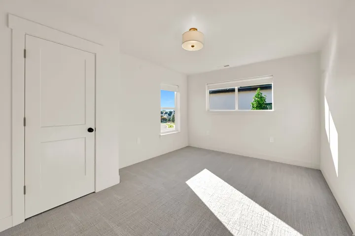 Neutral-toned room featuring light gray carpeting, two windows with white blinds, and a white two-panel door with black hardware
