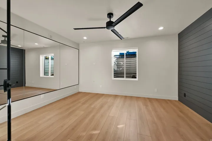Spacious room featuring wood-finish flooring, a full-wall mirror, recessed lighting, and a modern ceiling fan