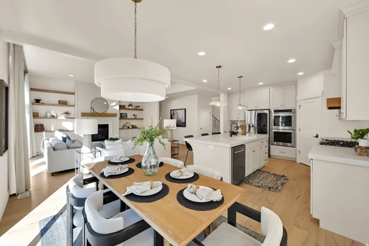 Open-concept living space featuring wood-finish flooring, a contemporary dining area with a tiered chandelier, and a kitchen with an oversized island and stainless steel appliances