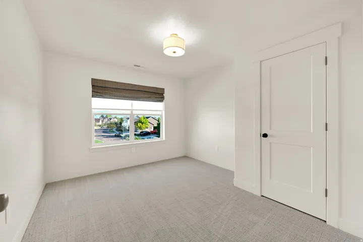 Bright room featuring a large window with a woven Roman shade, light-colored patterned carpeting, and white walls