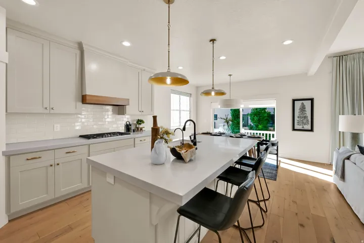 Kitchen featuring light-toned cabinetry, a white subway tile backsplash, and a built-in range hood with a wood accent