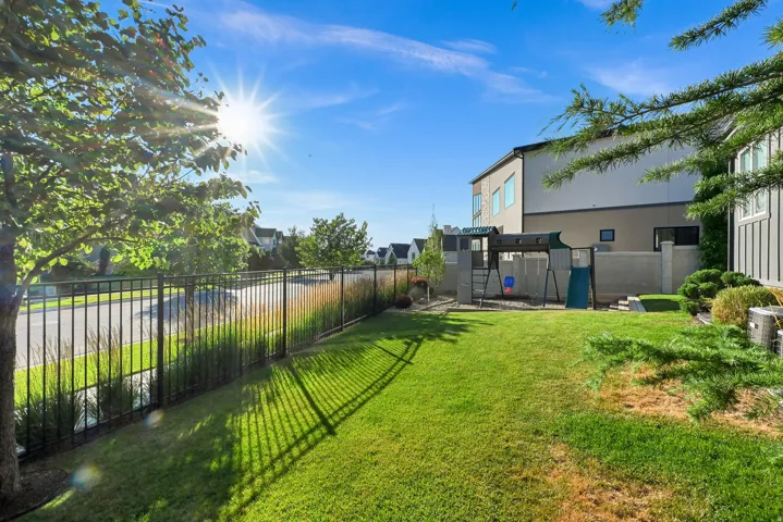 Expansive green lawn area featuring a black wrought iron fence, mature trees, and shrubs