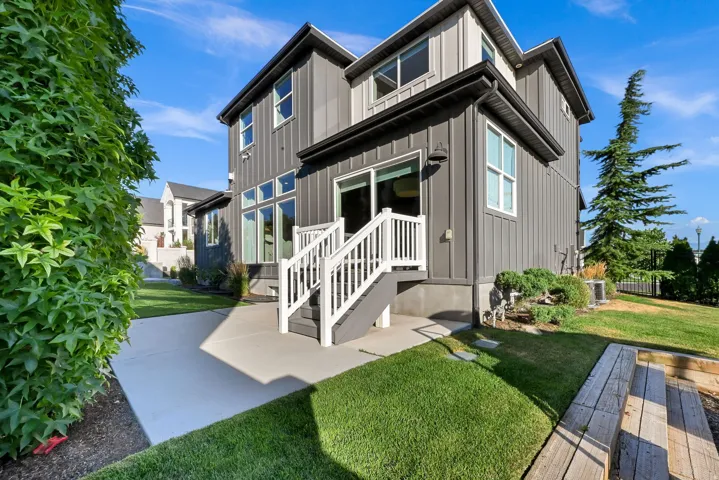 Rear exterior featuring board and batten siding, a concrete patio, a sliding glass door, white railings, and a tiered grassy area