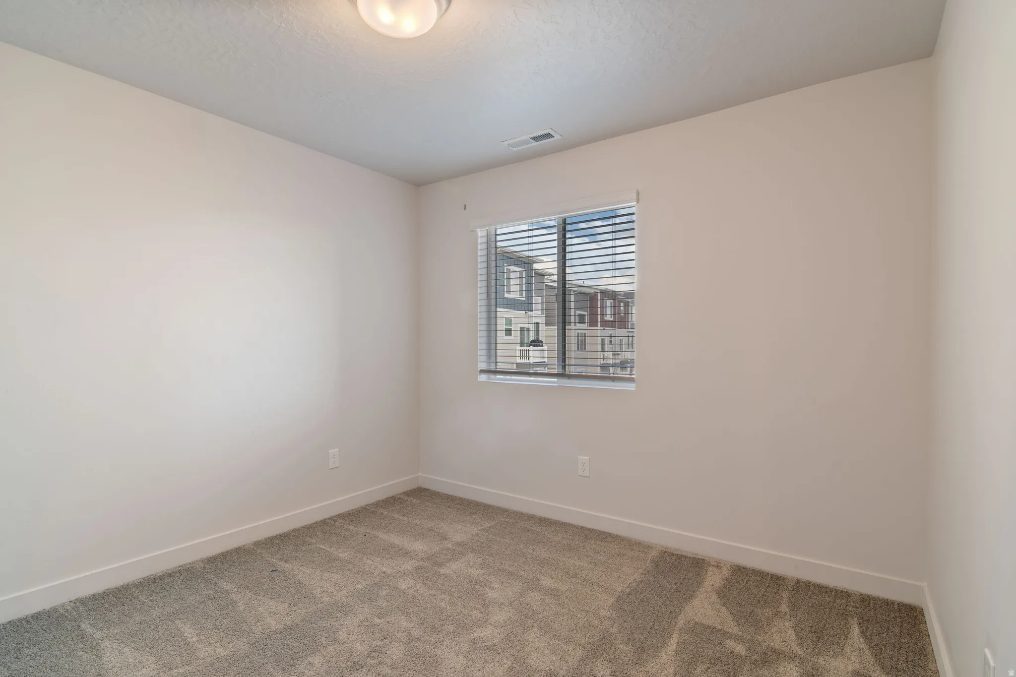 Carpeted room with a single window featuring blinds