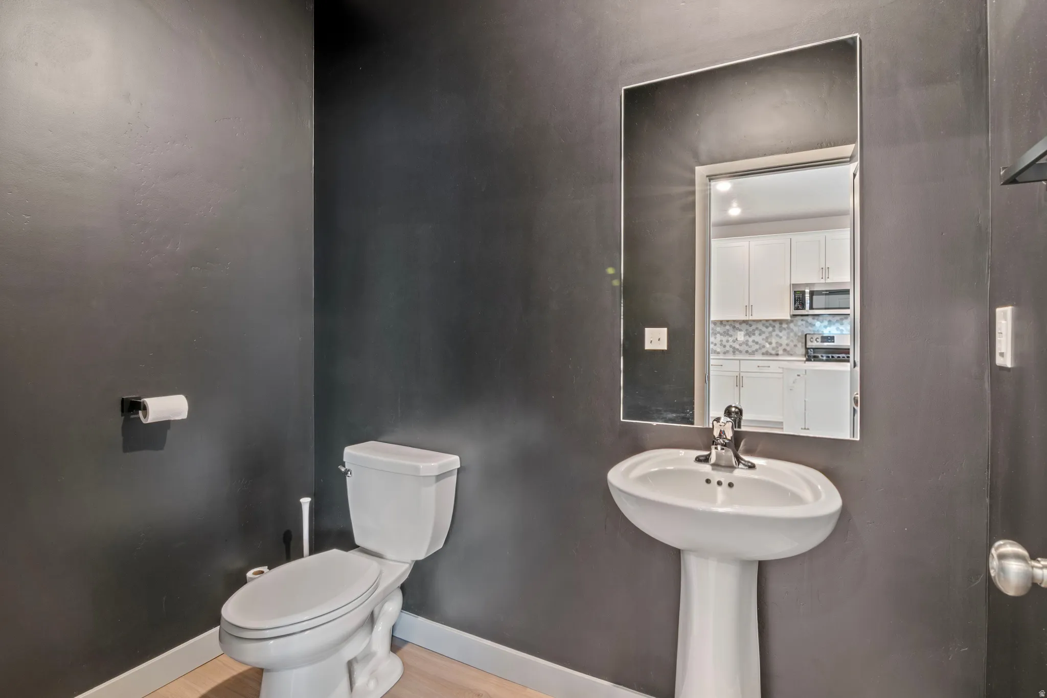 Compact powder room featuring a pedestal sink, white toilet, and dark-toned walls