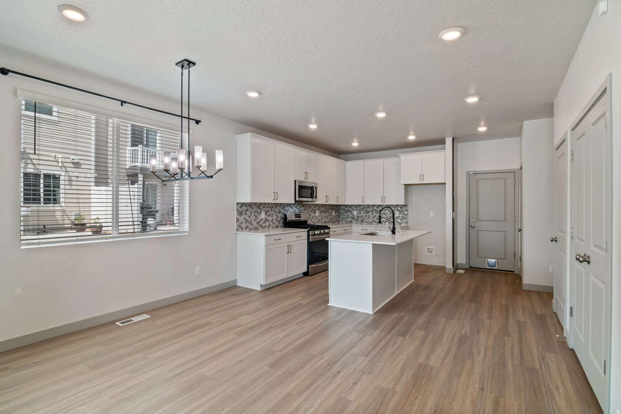 Open-concept living space with wood-finish flooring, recessed lighting, and a contemporary chandelier