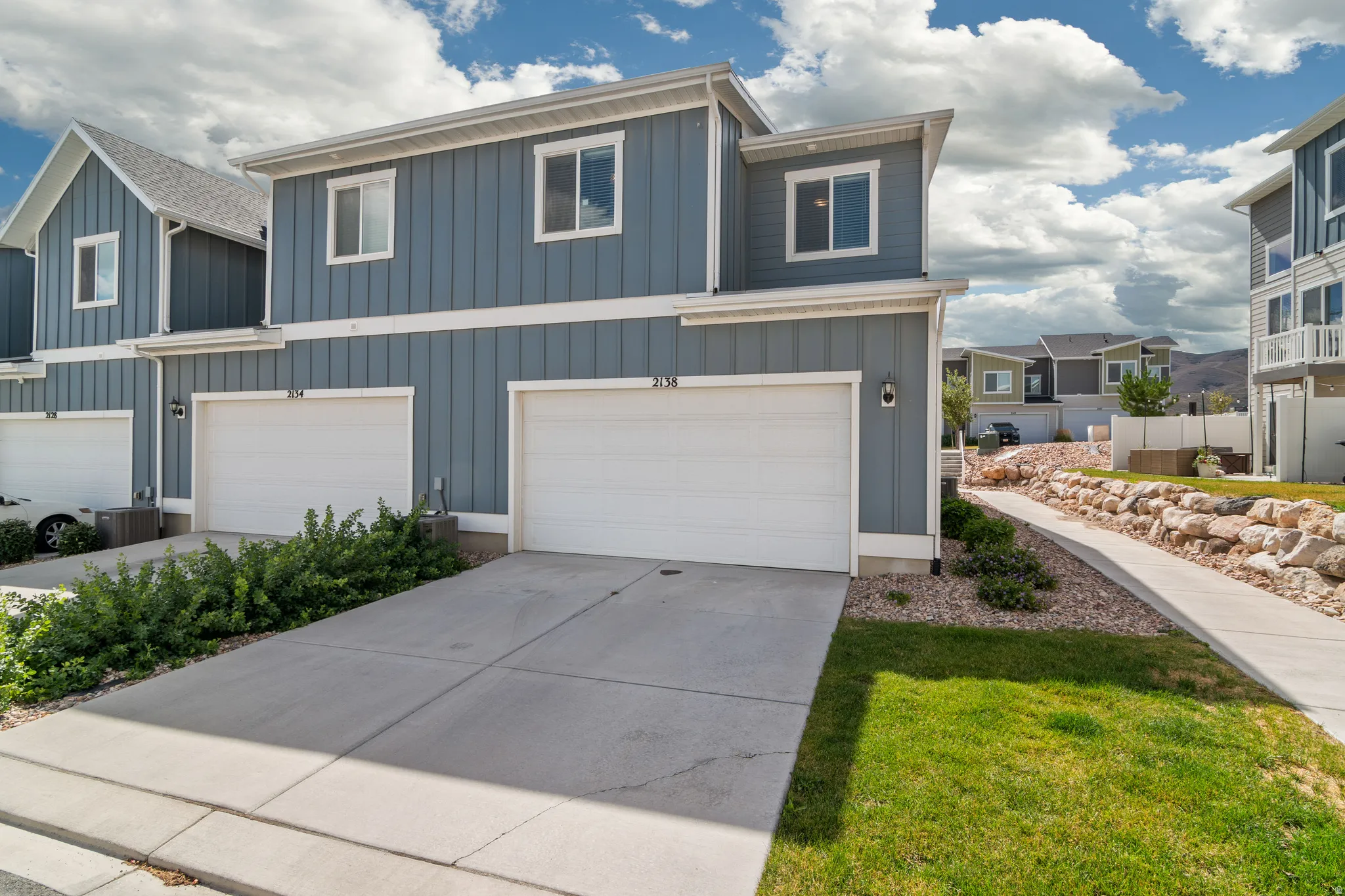 Modern townhome exterior featuring blue vertical siding, white trim, and a two-car garage with two-car driveway