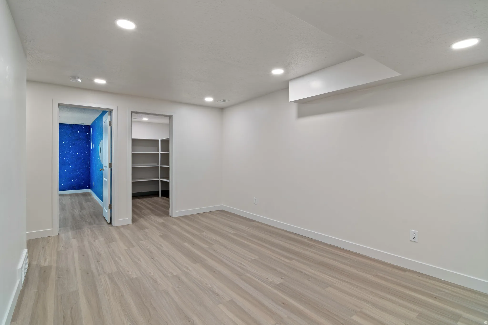 Spacious room featuring light wood-finish flooring and recessed lighting