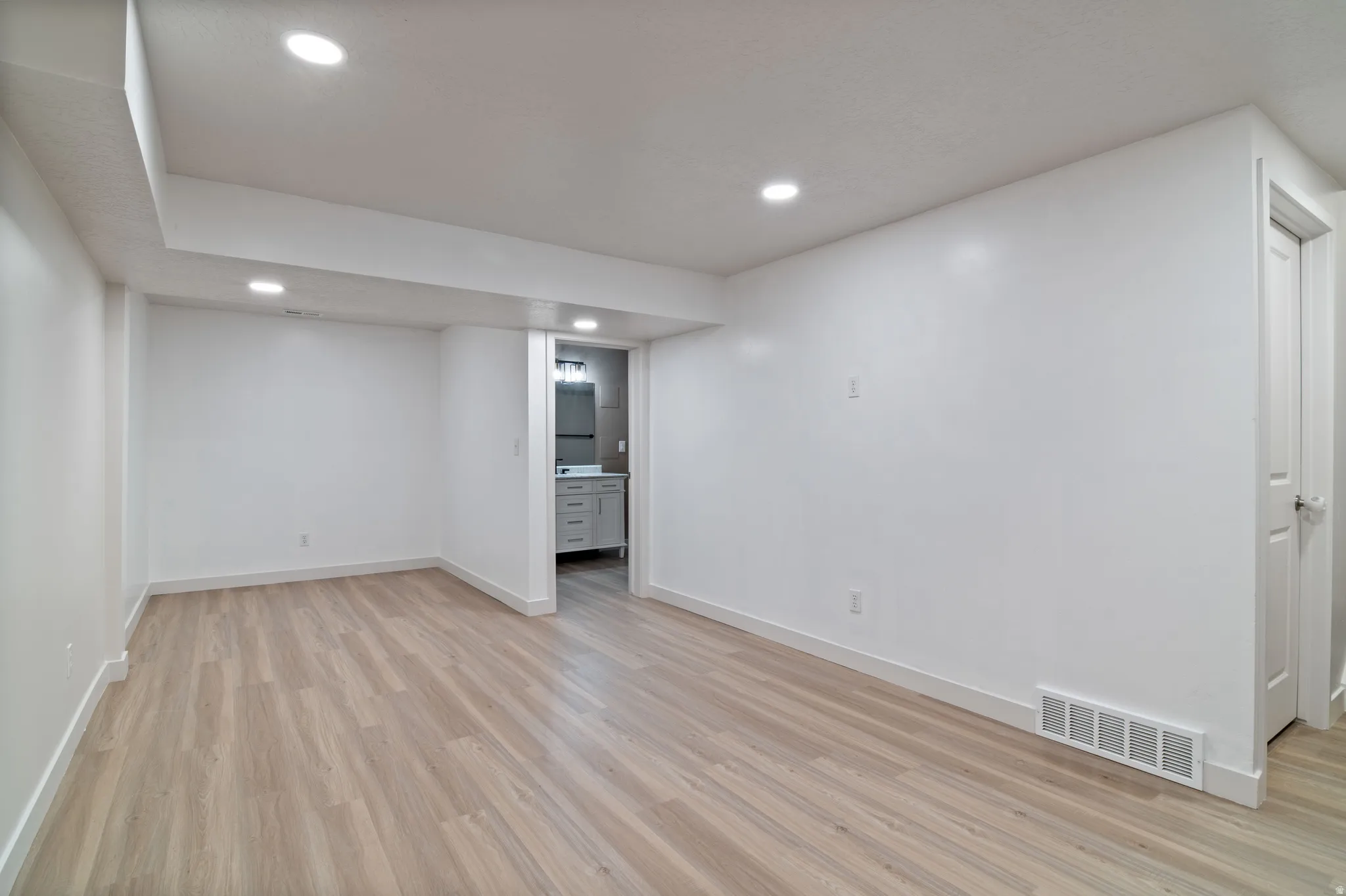 Spacious room featuring wood-finish flooring, recessed lighting, white walls, and white trim