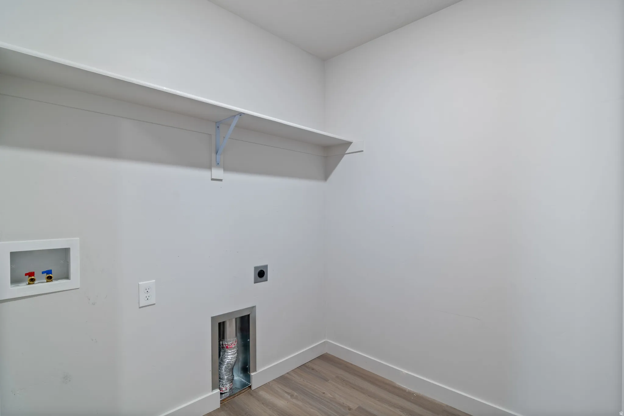 Utility area featuring light wood-finish flooring, white baseboards, and a wall-mounted white shelf with brackets
