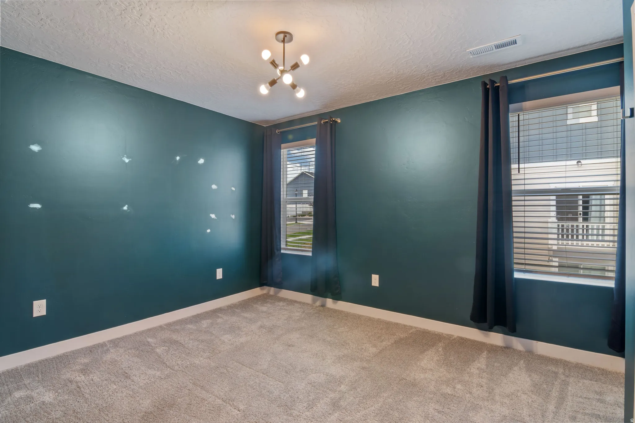 Spacious room featuring rich teal walls, two windows with blinds and dark curtains, and a contemporary ceiling light fixture