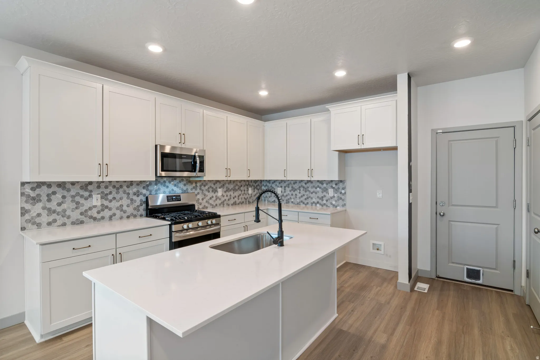 Modern kitchen featuring white shaker cabinetry, stainless steel appliances including a gas range and microwave, a hexagonal mosaic tile backsplash, and light-colored countertops