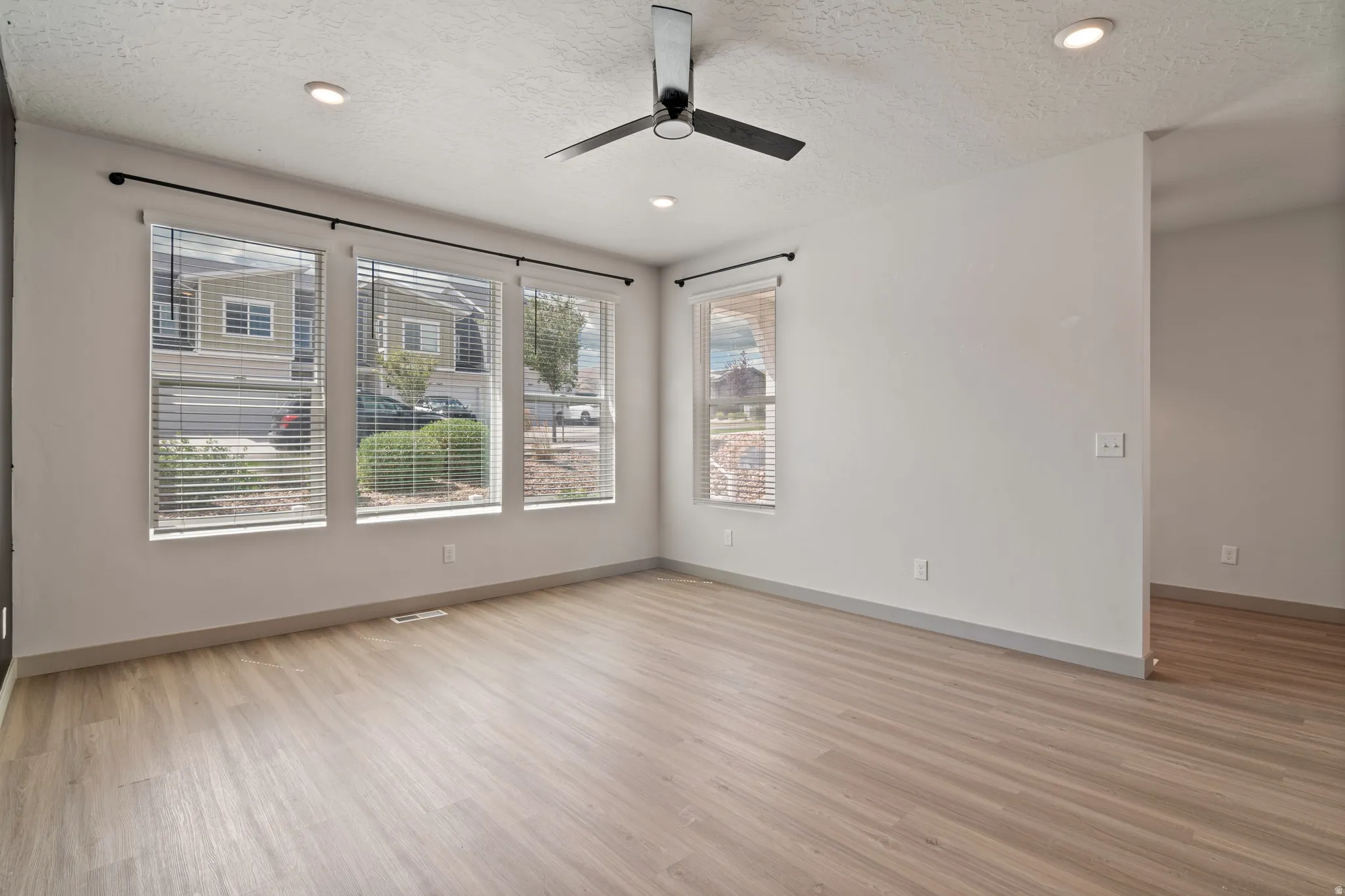 Bright living space featuring wood-finish flooring, recessed lighting, multiple windows with blinds, a modern ceiling fan, and painted baseboards