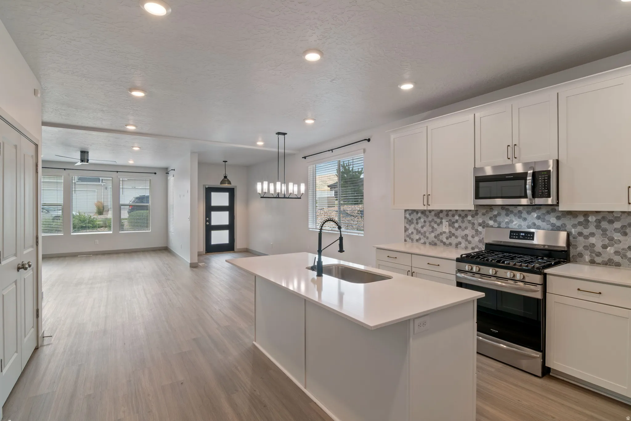 Open-concept kitchen and living area featuring light wood-finish flooring, recessed lighting, and a kitchen island with an undermount sink and matte black faucet