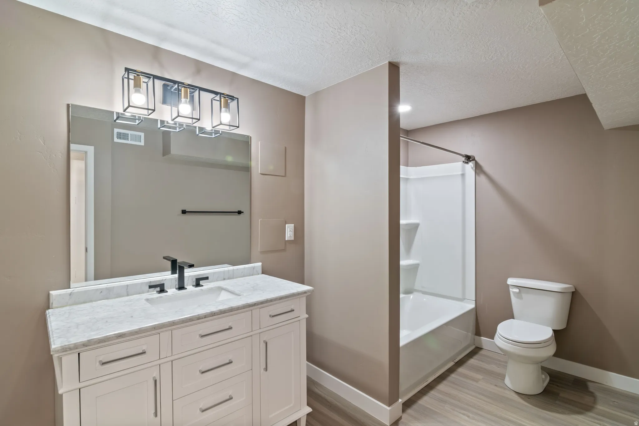 Full Bathroom featuring a white vanity with a light-toned countertop, a rectangular mirror, and a three-light fixture with black metal frames