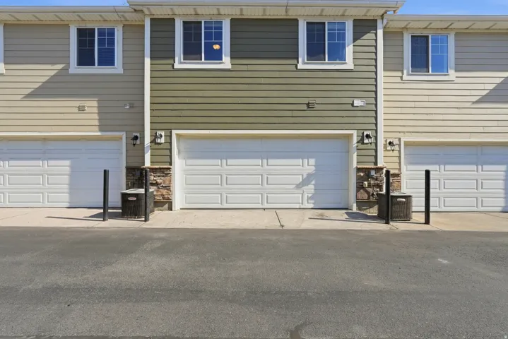 Multi-unit building exterior featuring horizontally-oriented siding in varied tones, white framed windows, and individual garage access