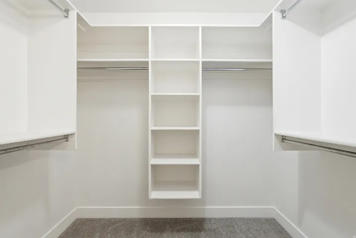 Walk-in closet with integrated shelving, multiple hanging rods, white walls, white baseboards, and carpet flooring