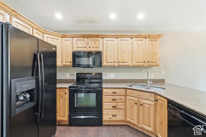 Kitchen featuring light wood cabinetry with dark hardware, stone-finish countertops, and wood-finish flooring