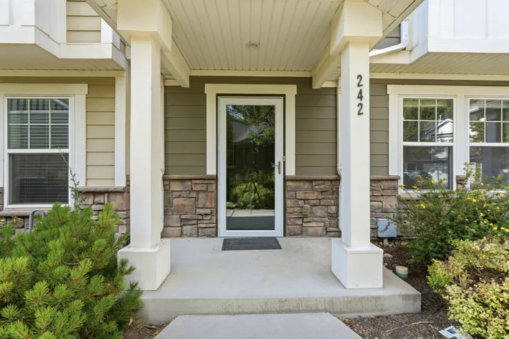 Inviting front entry featuring a storm door, stone veneer accents, siding exterior, and white structural columns