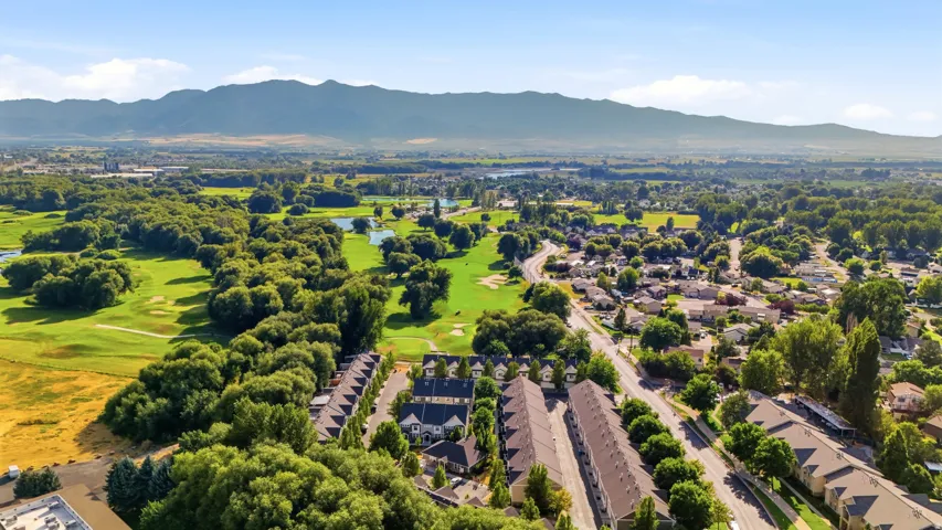 Aerial perspective showcasing residential properties bordering a golf course with mountainous backdrop