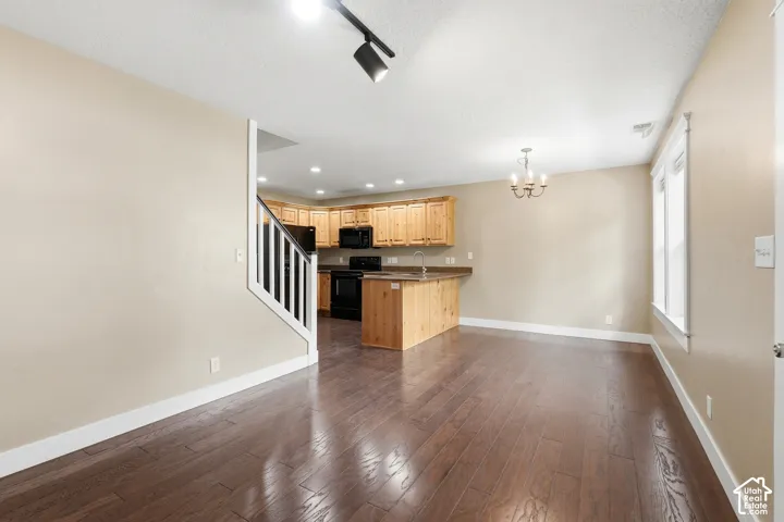 Open-concept living area featuring wood-finish flooring, a contemporary track lighting fixture, and a staircase with white risers and dark handrails