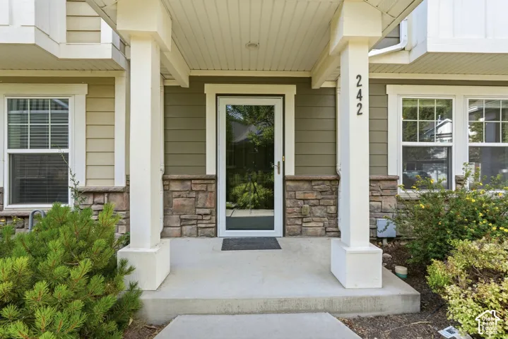 Inviting front entry featuring a storm door, stone veneer accents, siding exterior, and white structural columns
