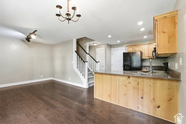Open-concept living area featuring rich wood-finish flooring, a contemporary chandelier, and a staircase with dark wood handrails and white balusters