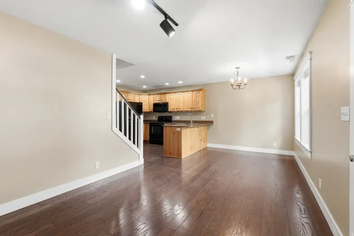 Open-concept living area featuring wood-finish flooring, a contemporary track lighting fixture, and a staircase with white risers and dark handrails