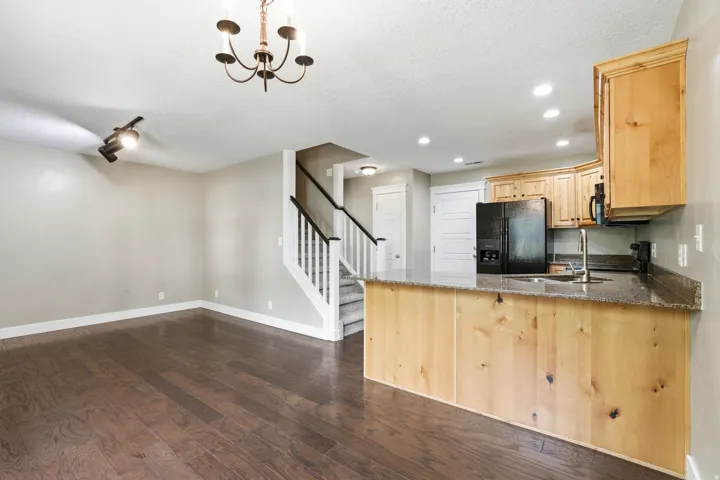 Open-concept living area featuring rich wood-finish flooring, a contemporary chandelier, and a staircase with dark wood handrails and white balusters