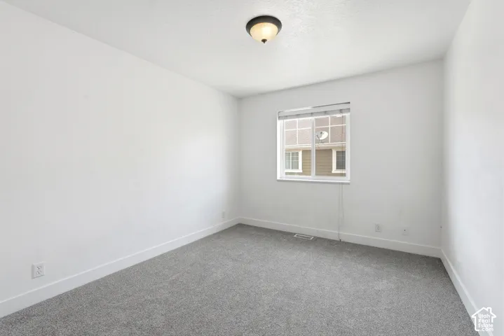 Light-filled room featuring neutral gray carpeting, white walls, white baseboards, a single window with blinds, and a ceiling-mounted light fixture