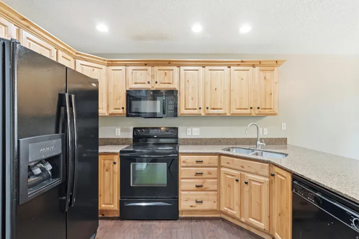 Kitchen featuring light wood cabinetry with dark hardware, stone-finish countertops, and wood-finish flooring