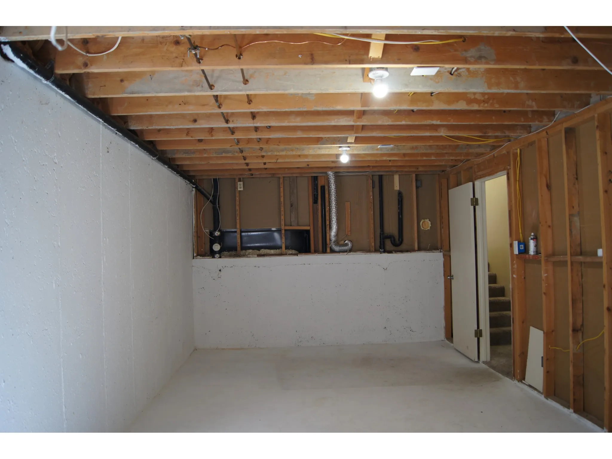 Unfinished basement space featuring exposed wooden ceiling joists, concrete flooring, painted foundation walls, and visible utility lines