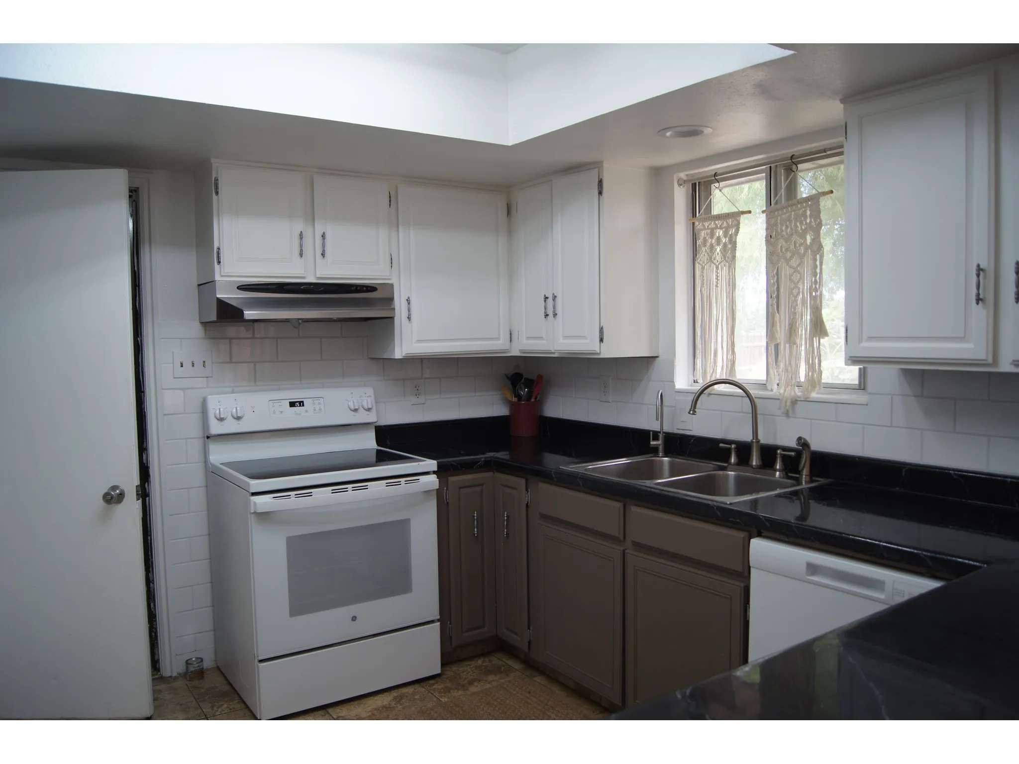 Kitchen featuring white upper cabinetry, white subway tile backsplash, dark countertops, a double basin stainless steel sink, and a white electric range