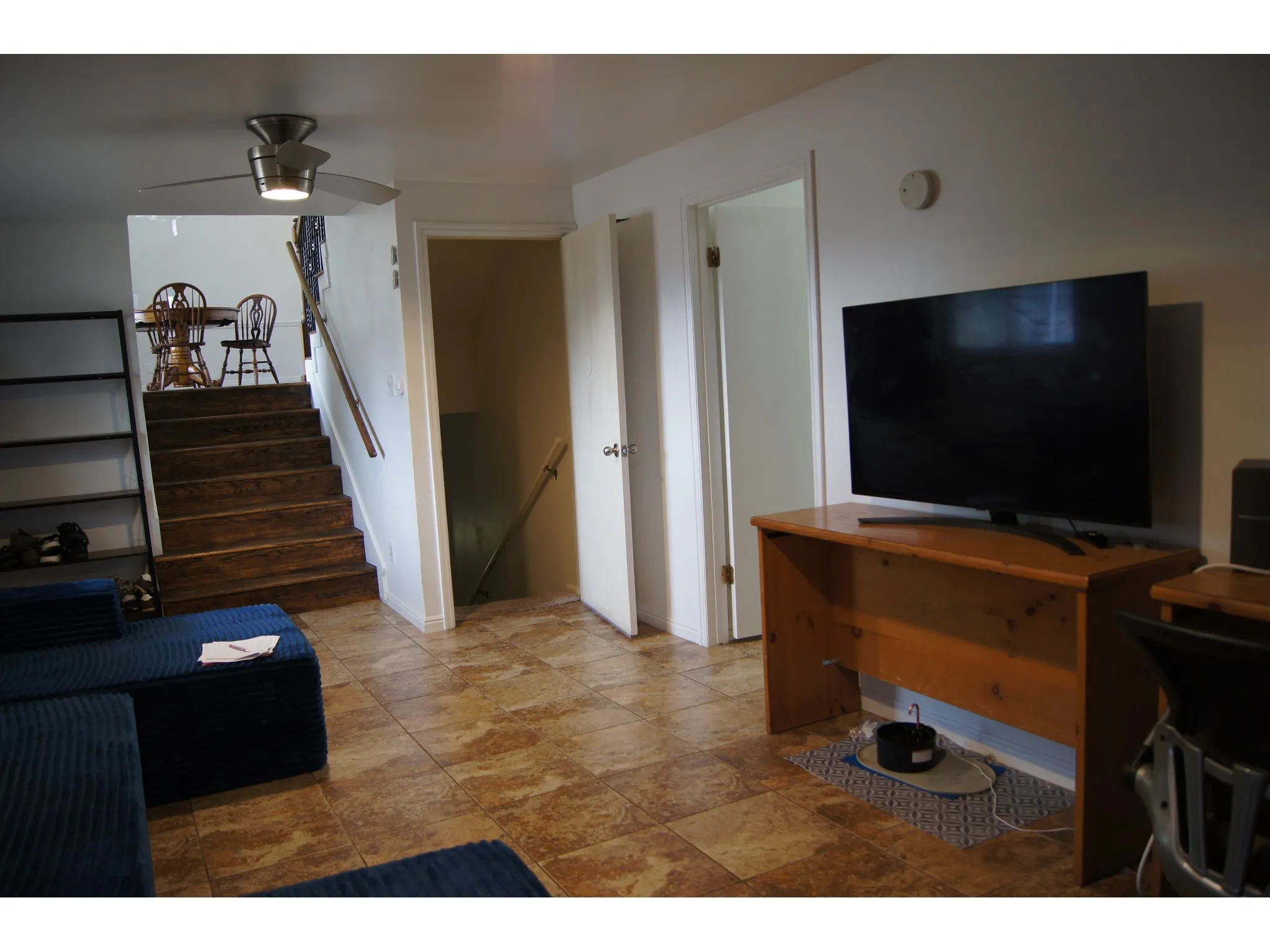 Lower level living area featuring tile flooring, wood-finish stairs, a ceiling fan with integrated lighting, and a built-in shelving unit