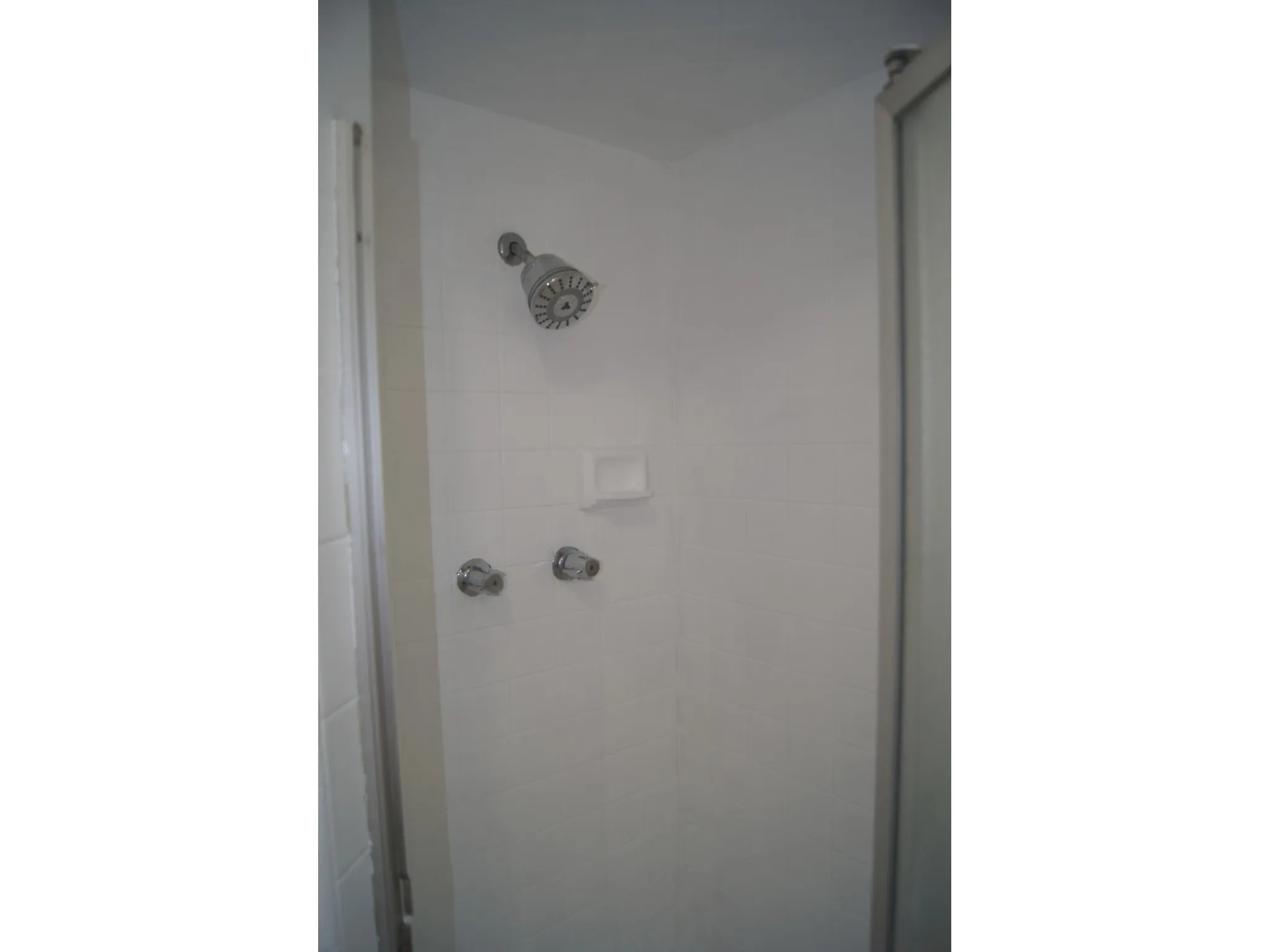Master Bedroom Shower enclosure featuring white tile walls, chrome showerhead, and matching chrome controls